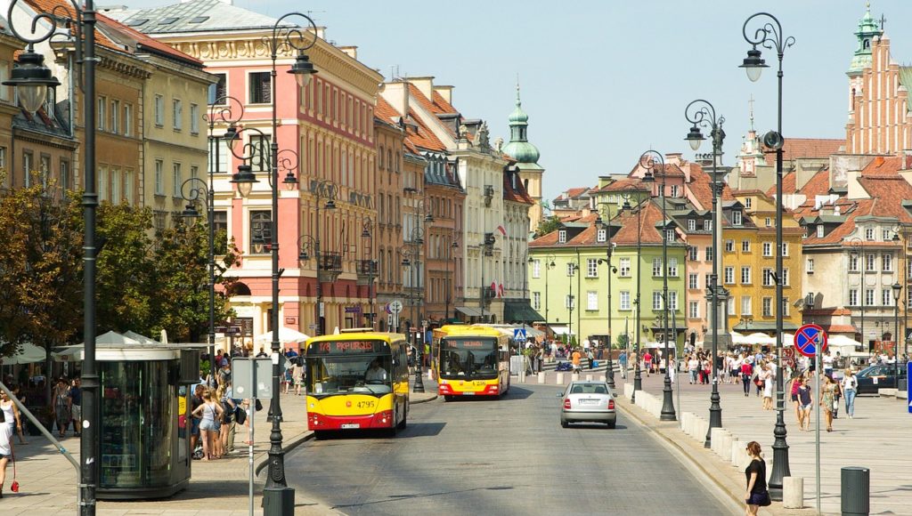 Dwa żółto-czerwone autobusy na ulicy Krakowskie Przedmieście. W tle plac Zamkowy. Fot. Pixabay