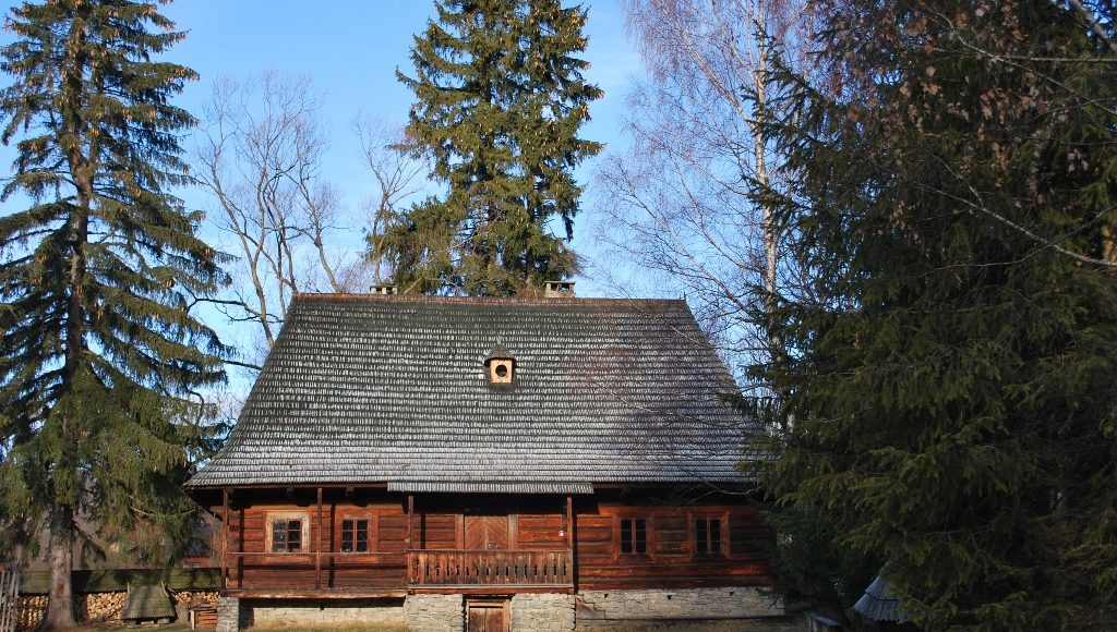 chata ze skansenu, naokoło niej drzewa iglaste