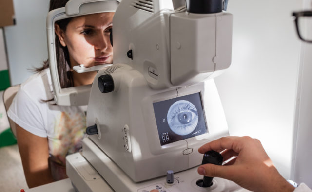 kobieta siedzi przed maszyną do badania gałek ocznych
