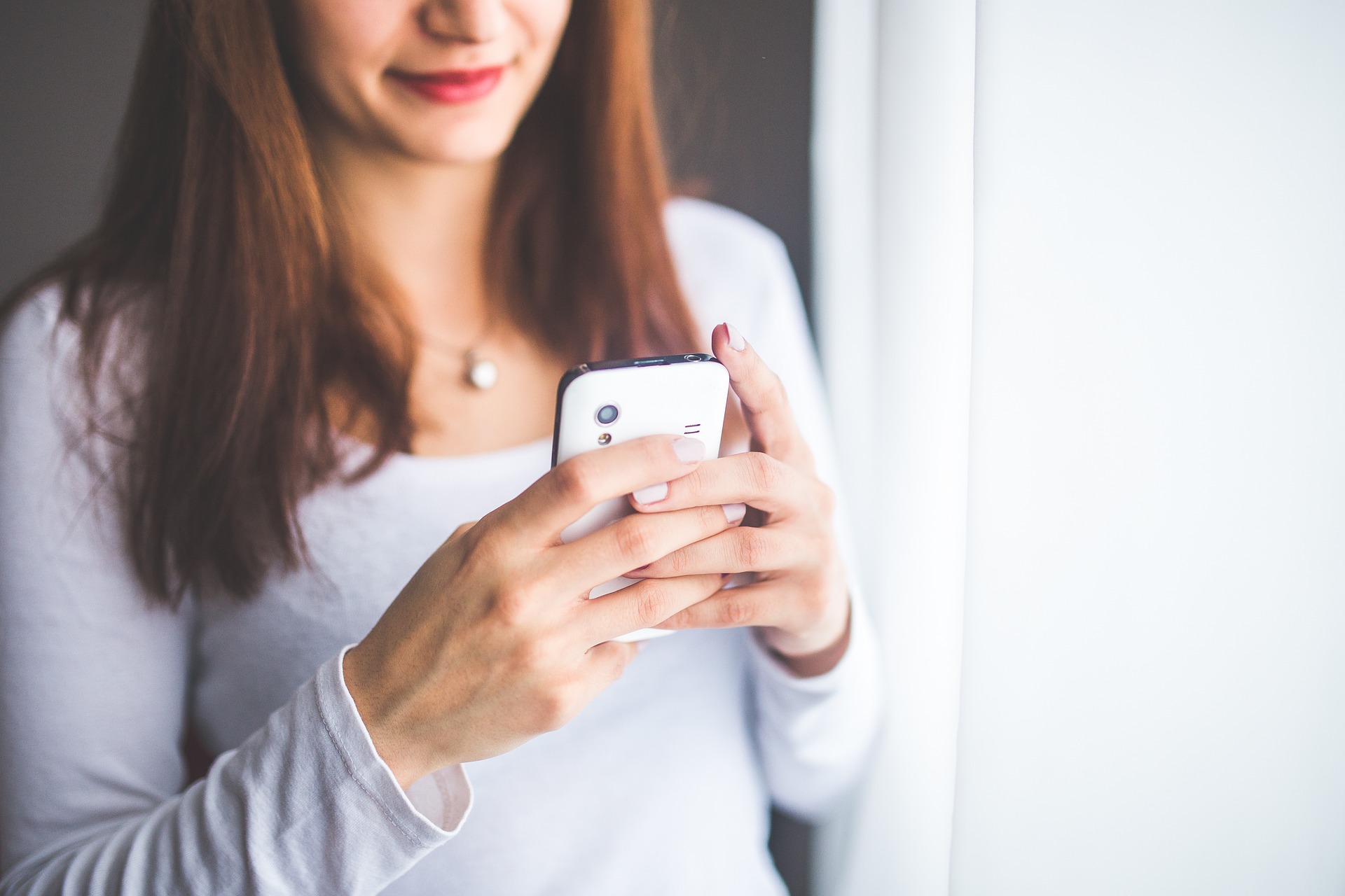 kobieta trzyma telefon zwrócony w swoją stronę, widać tylko dolną połowę jej twarzy oraz korpus
