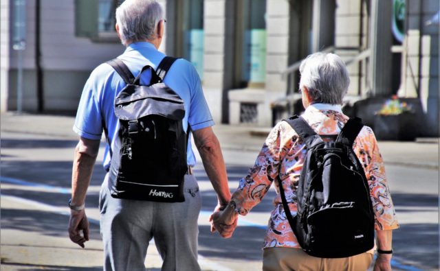 Dwoje seniorów - kobieta i mężczyzna - podczas spaceru. Trzymają się za ręce.