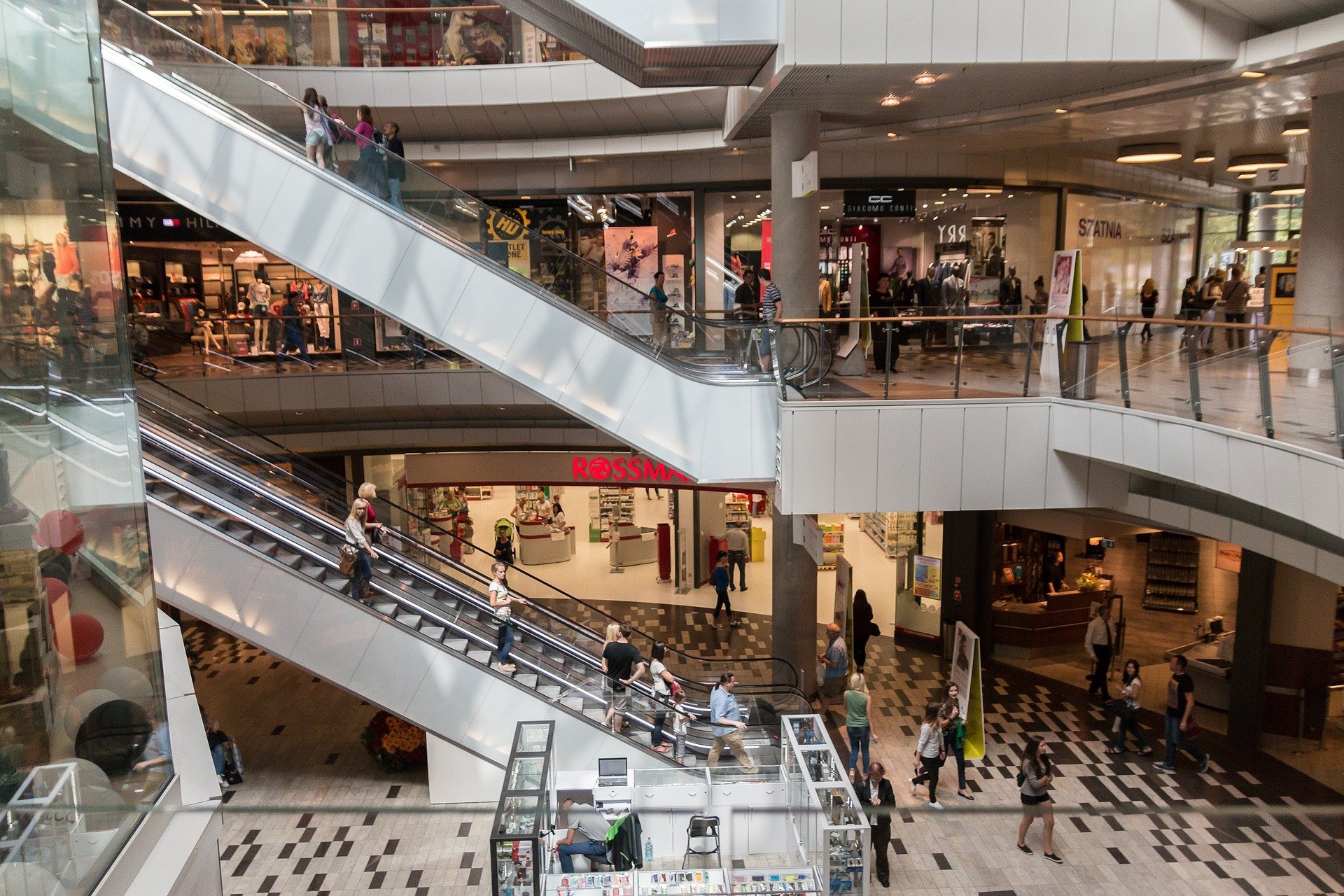 widok na galerię handlową, widać witryny sklepowe, ruchome schody i tłum ludzi na schodach i na korytarzach