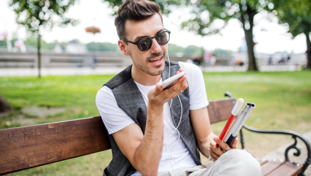 Młody mężczyzn z białą laską słucha podcastu ze smartfona
