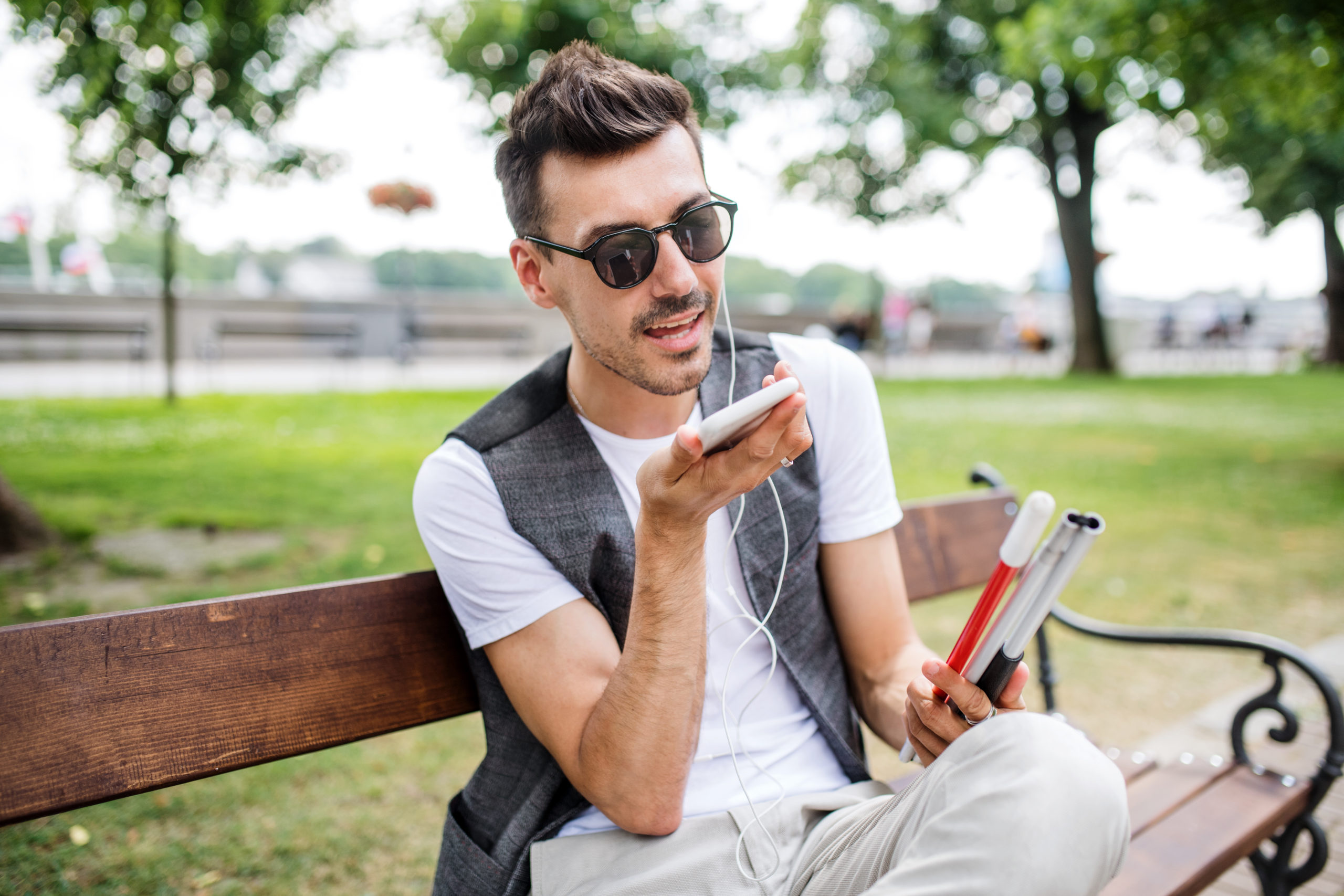 Młody mężczyzn z białą laską słucha podcastu ze smartfona