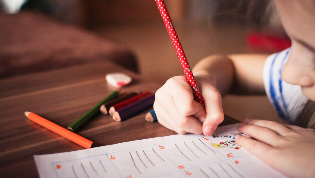 dziecko siedzi przy biurku i coś rysuje, widzimy tylko część jego twarzy z prawej strony, zbliżenie na kartkę papieru, na której jest rysunek