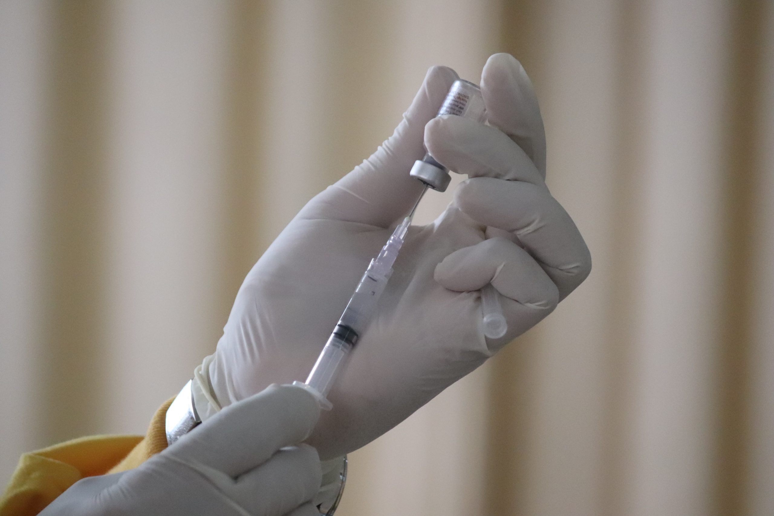 Widok na dłonie lekarza, który wkłada strzykawkę do ampułki ze szczepionką