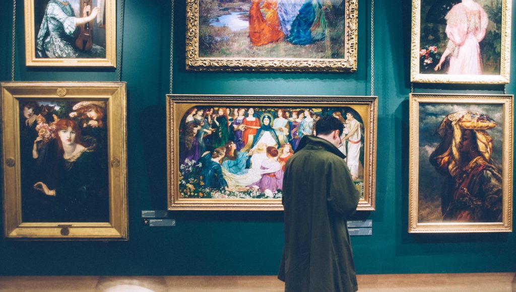 mężczyzna stoi w muzeum, ogląda obrazy, które wiszą przed nim na ścianie