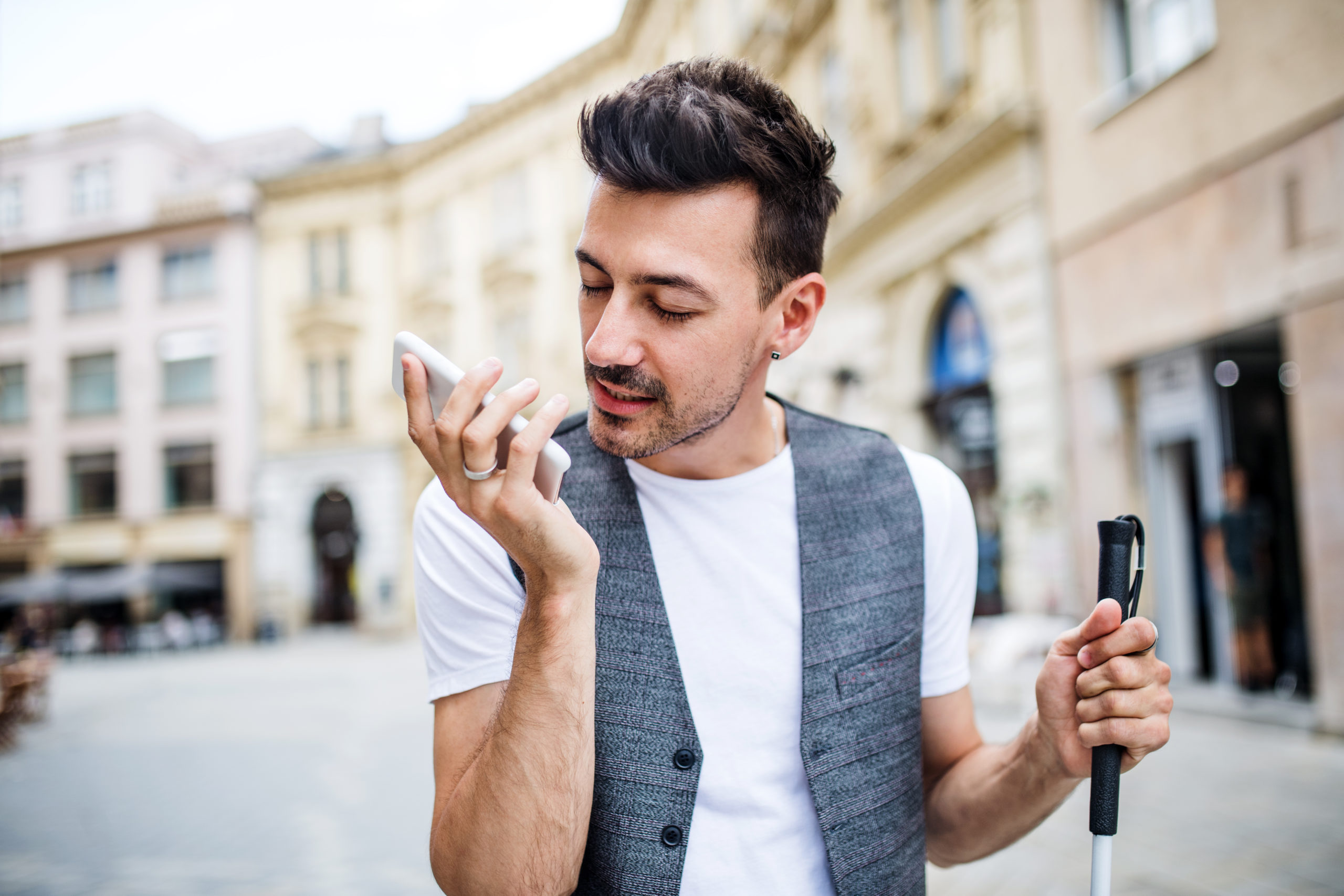 Niewidomy męzczyzna idzie ulicą odsłuchuje komunikaty ze smartfona