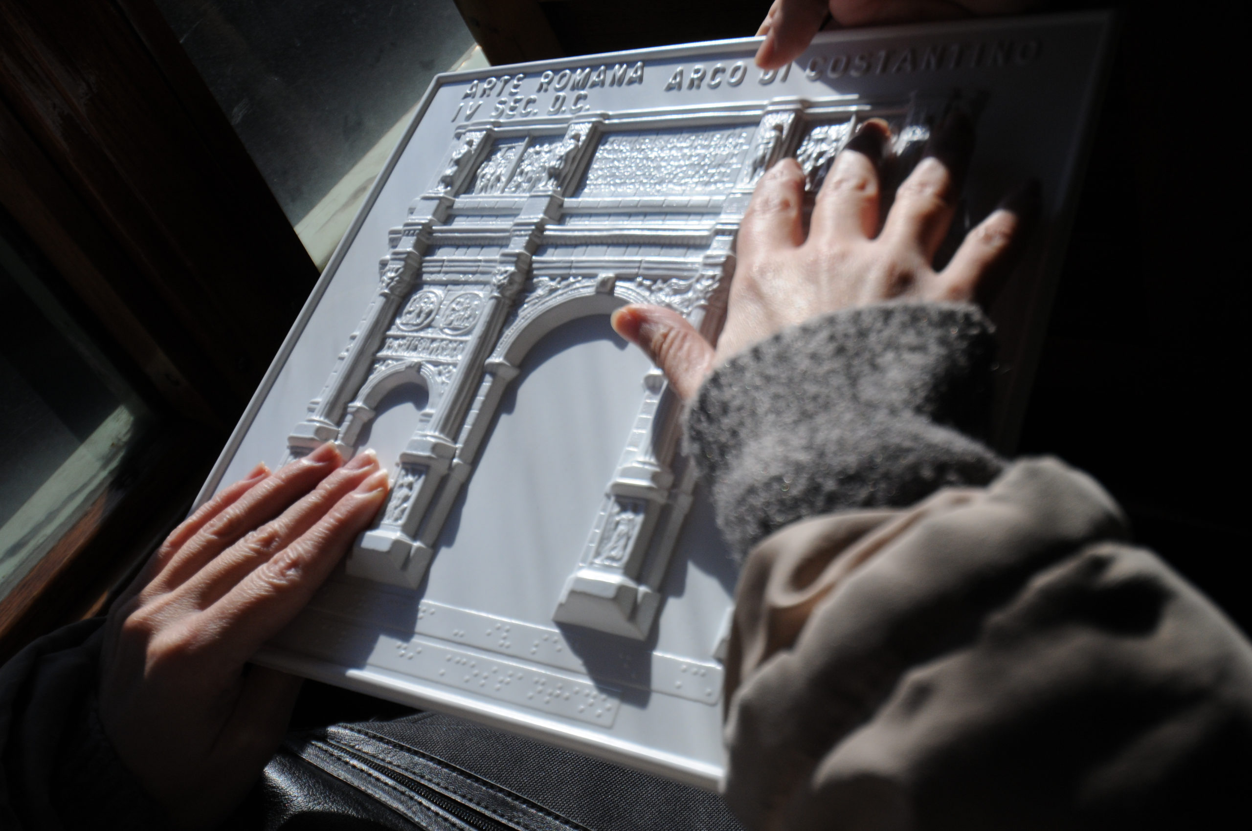 Osoba niewidoma palcami bada tyflografikę przedstawiającą zabytkową bramę