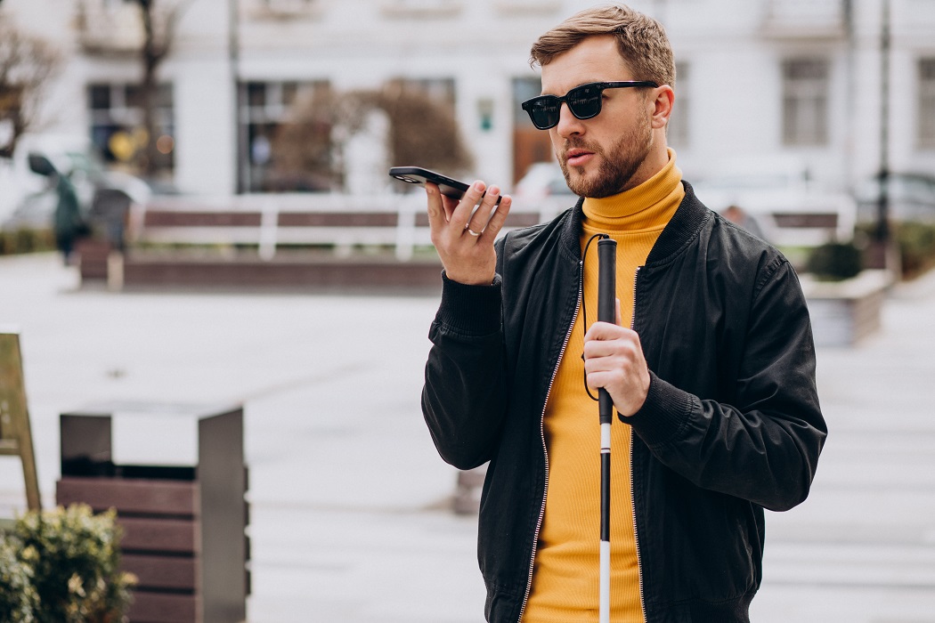 Niewidomy mężczyzna słucha nagrania ze smartfonu będąc na ulicy w mieście