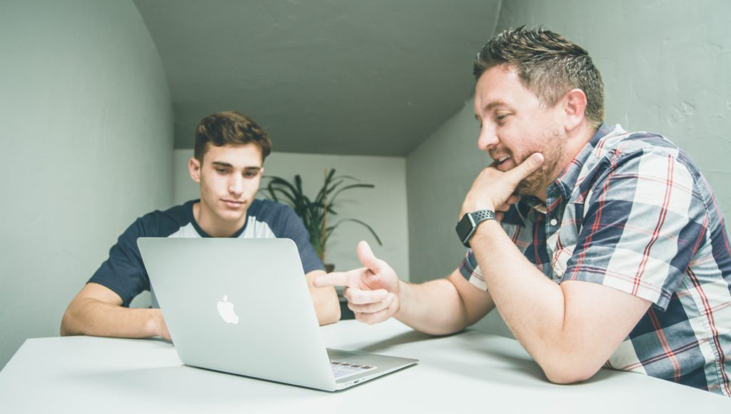 Dwóch mężczyzn omawia jakąś sprawę przy stole, patrzą na ekran laptopa