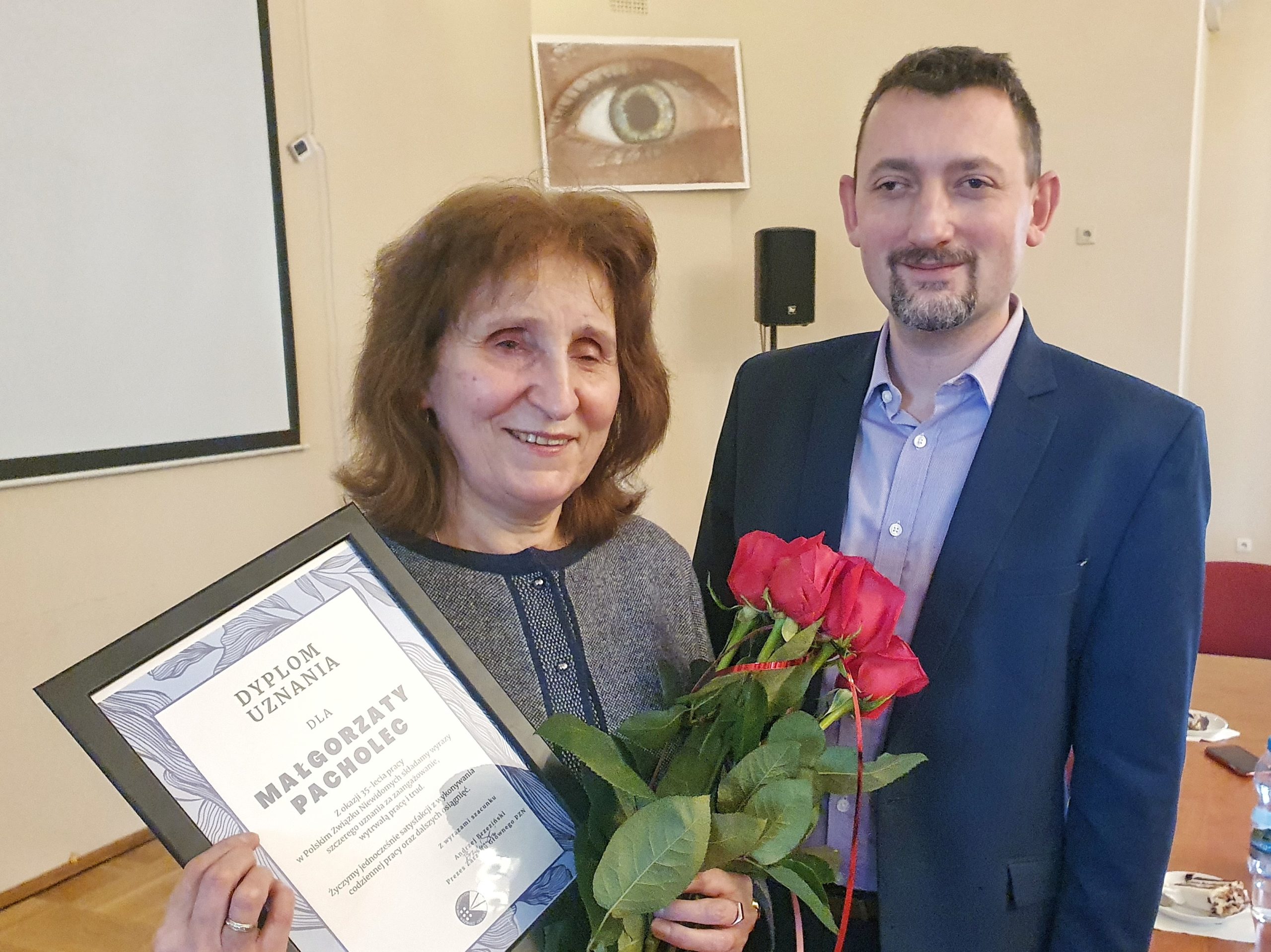 Małgorzata Pacholec z dyplomem i kwiatami, obok prezes Andrzej Brzeziński