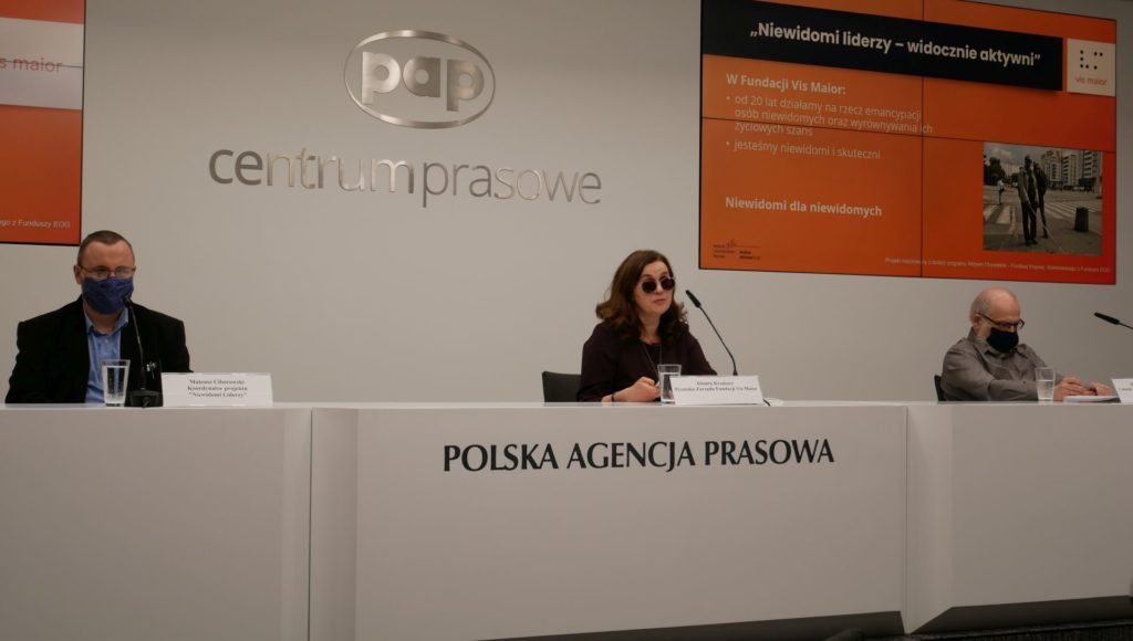 Mateusz Ciborowski, Jolanta Kramarz oraz Dariusz Kupiecki siedzą za dużym stołem w sali konferencyjnej. Za nimi widinieje logo PAP oraz prezentacja multimedialna na temat fundacji Vis Maior