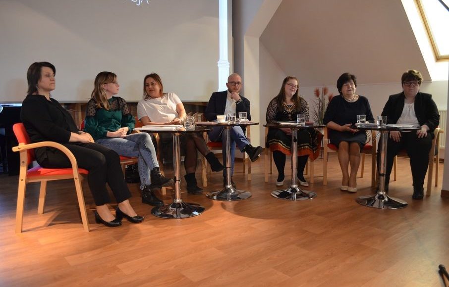 uczestnicy wydarzenia siedzą przy stolikach w bibliotece