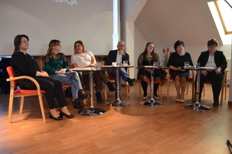 uczestnicy wydarzenia siedzą przy stolikach w bibliotece