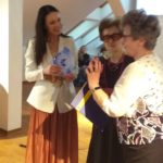 Wiesława Krych stoi i mówi coś do mikrofonu obok niej stoi Izabela Bocheńska, uśmiecha się i trzyma statuetkę, w tle siedzą poeci