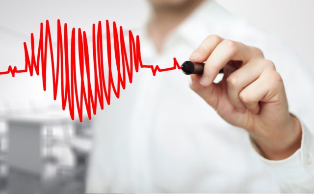 zbliżenie na rękę lekarza, który trzyma czerwony mazak i rysuje linie podobne do zapisu ekg, któr układają się w kształt serca