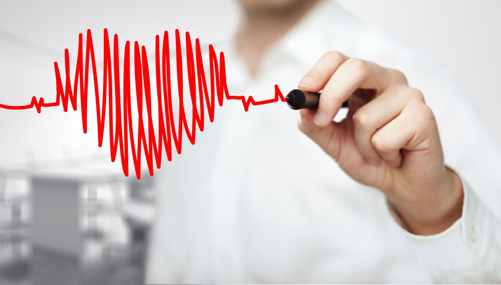 zbliżenie na rękę lekarza, który trzyma czerwony mazak i rysuje linie podobne do zapisu ekg, któr układają się w kształt serca