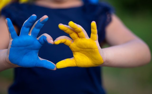 Dłonie dziecka ułożone w kształt serca. Jedna - w kolorze niebieskim, druga - żółtym.