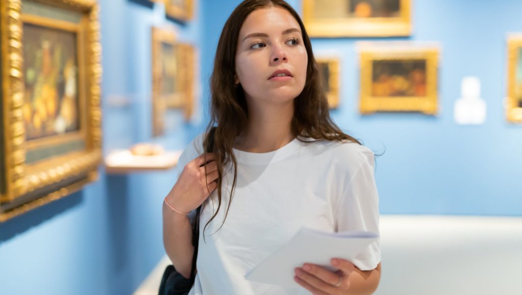 dziewczyna stoi w muzeum i się rozgląda, za nią na ścianach wiszą obrazy