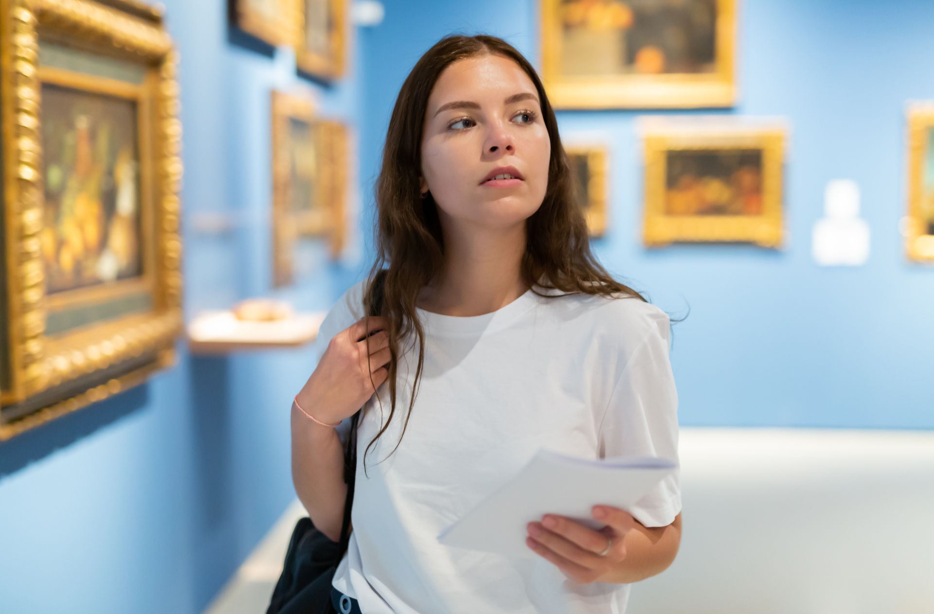 dziewczyna stoi w muzeum i się rozgląda, za nią na ścianach wiszą obrazy