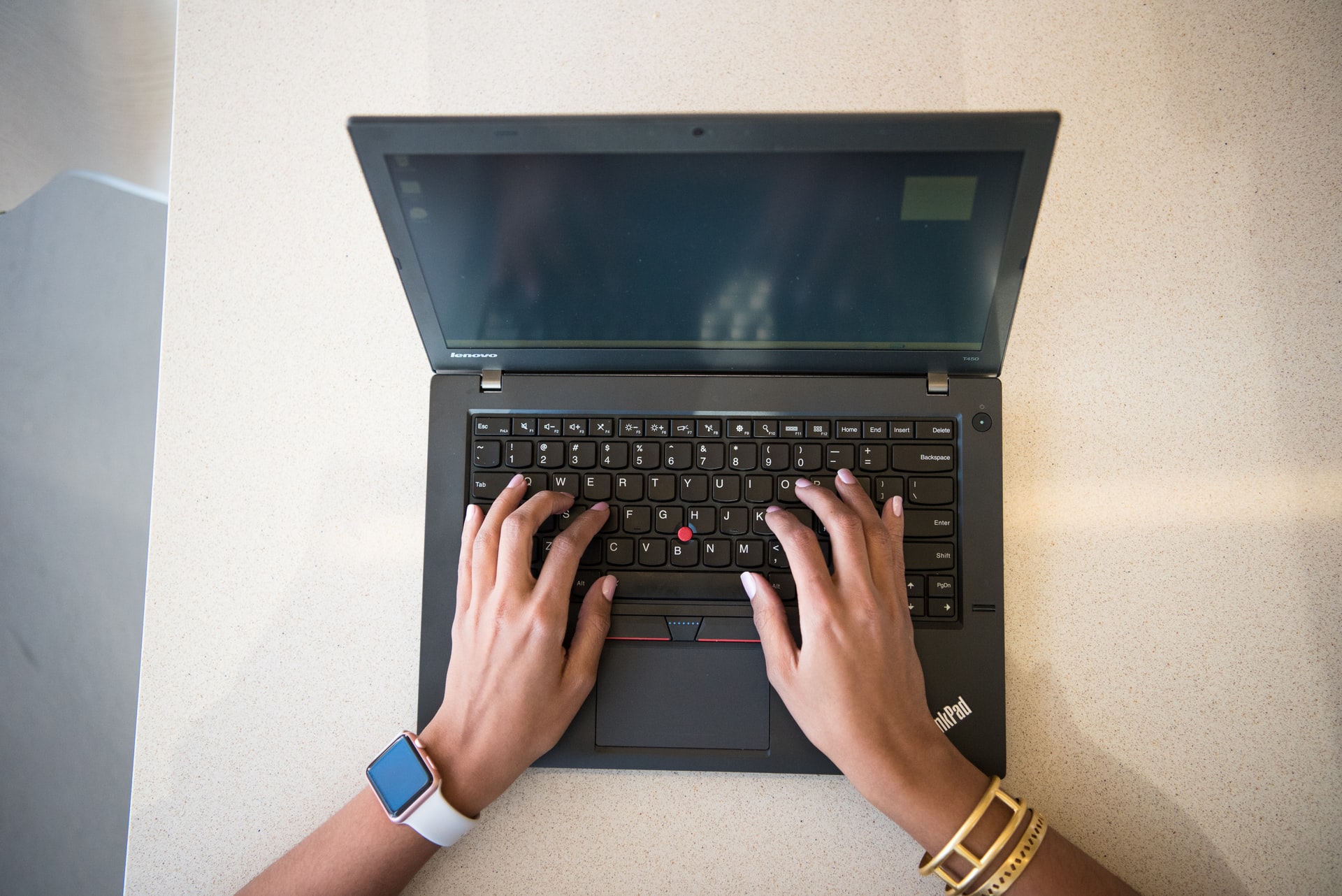 Zdjęcie zrobione z góry. Na biurku znajduje się laptop i dłonie kobiety piszące na klawiaturze.
