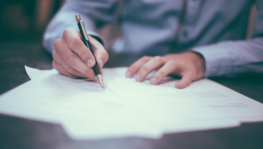 mężczyzna siedzi przy stole i pisze coś na kartce papieru, zbliżenie tylko na jego ręce