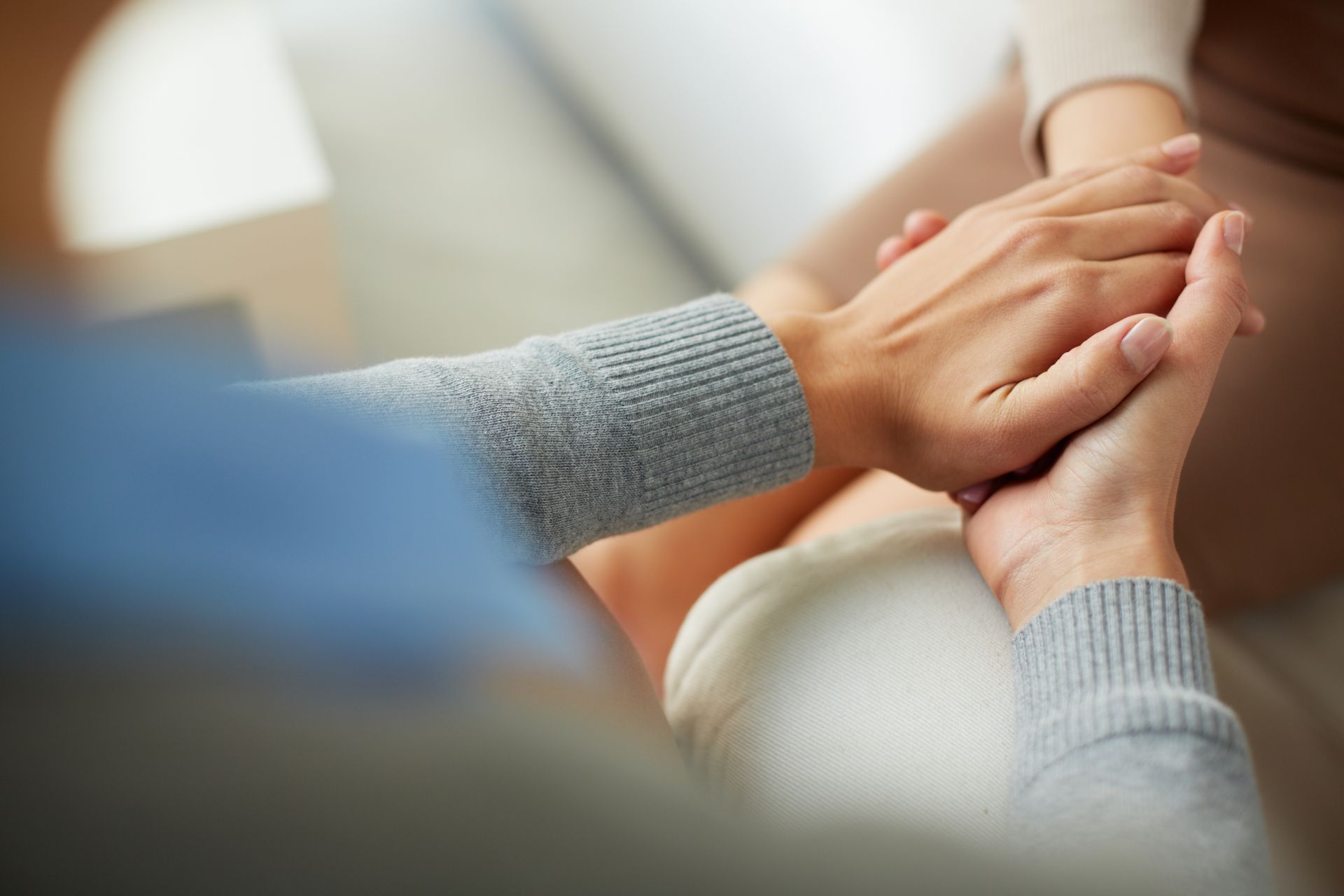 jedna osoba trzyma drugą za ręce w opiekuńczym geście, zbliżenie na ręce, nie widać twarzy tych osób