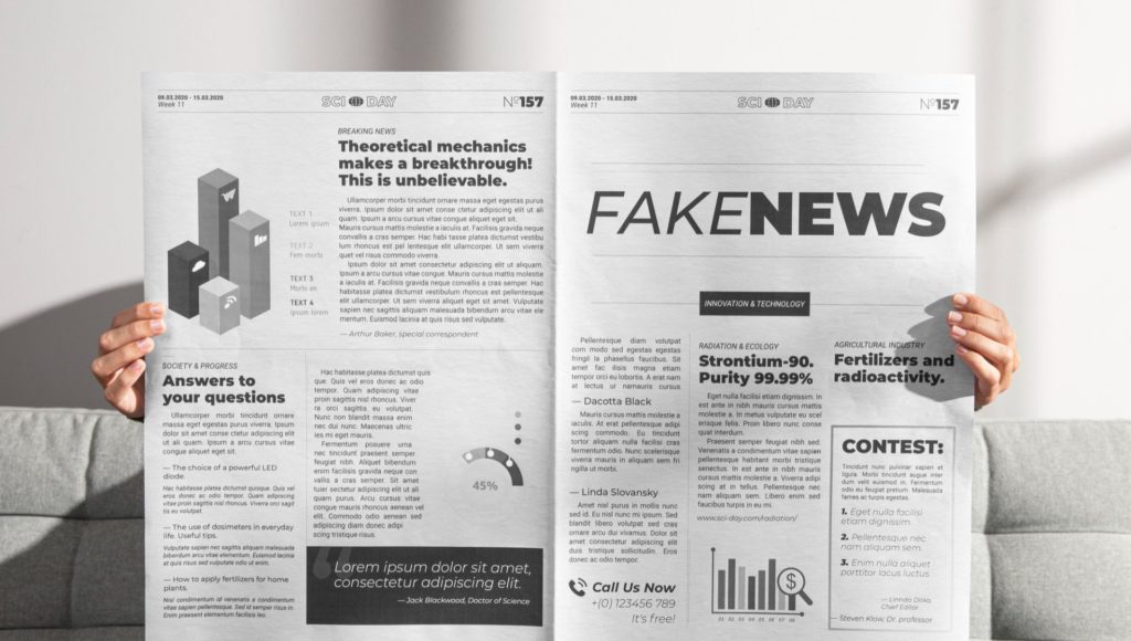 osoba siedzi na kanapie i trzyma rozłożoną gazetę, nie widać jej twarzy, tylko dłonie trzymające gazetę, na której widnieje wielki napis "fake news"