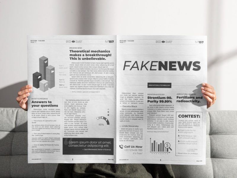 osoba siedzi na kanapie i trzyma rozłożoną gazetę, nie widać jej twarzy, tylko dłonie trzymające gazetę, na której widnieje wielki napis "fake news"