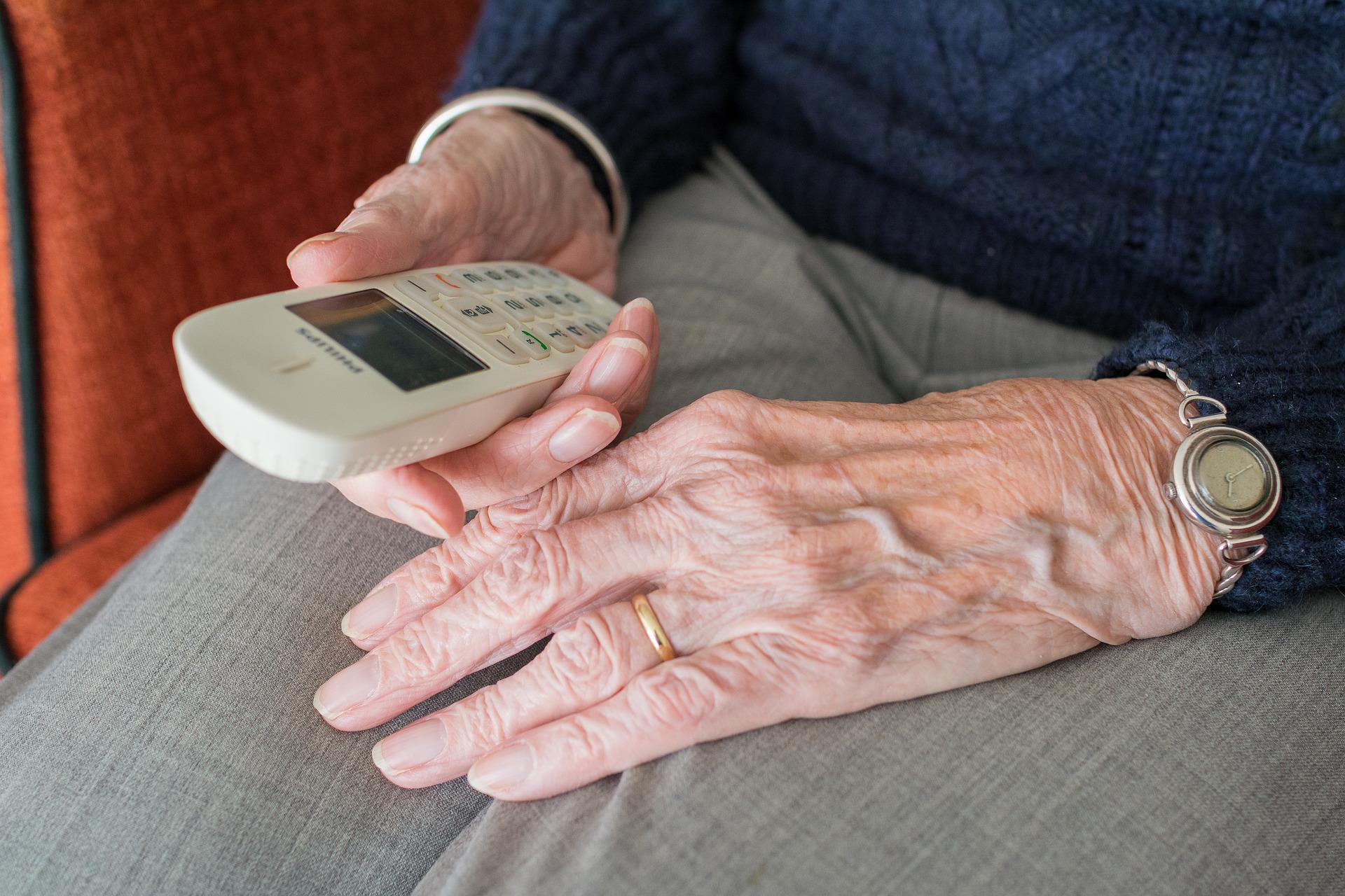 starsza osoba siedzi i trzyma w rękach telefon, nie widać jej twarzy, zbliżenie na ręce i telefon