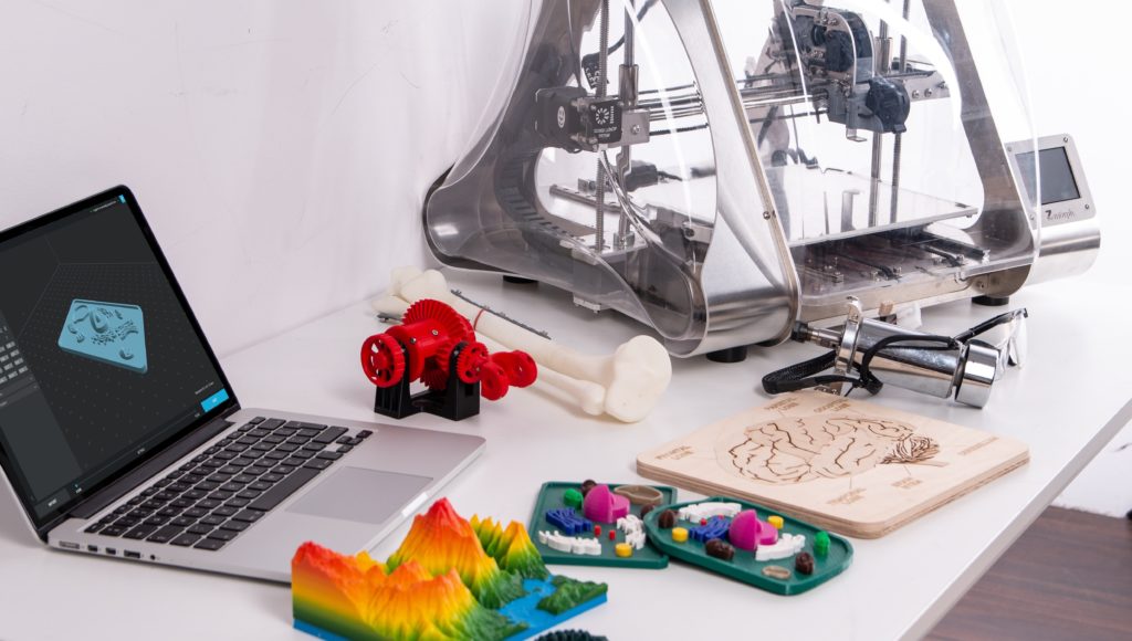 Druk 3D, drukarka na stole a obok wykonane modele