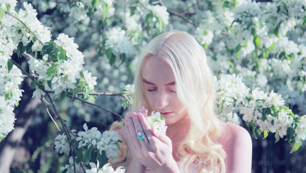 Młoda kobieta, która trzyma gałązkę drzewa i wącha znajdujące się na niej kwiaty.