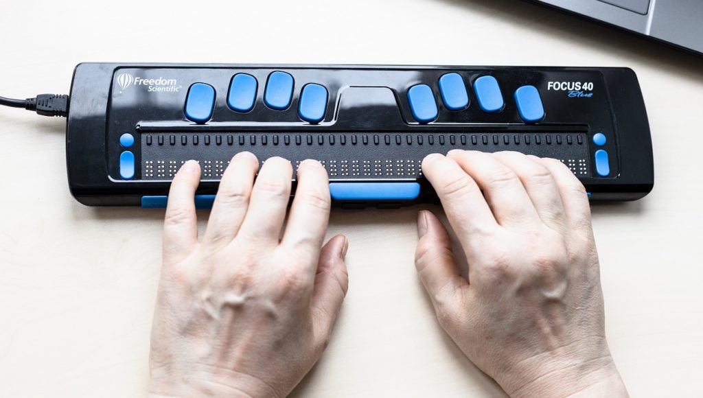 Ujęcie na ręce osoby piszącej na klawiaturze dla niewidomych