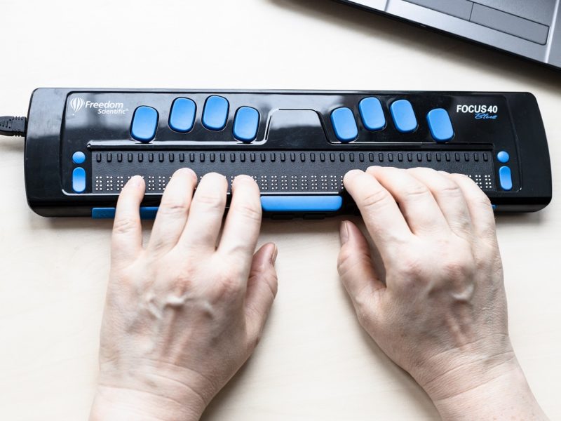 Ujęcie na ręce osoby piszącej na klawiaturze dla niewidomych