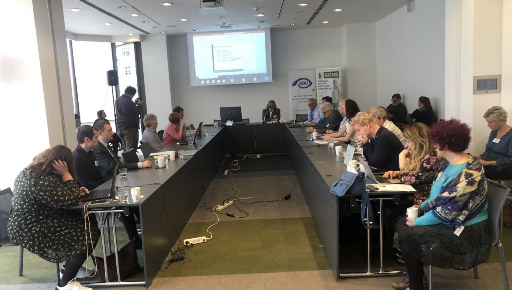 Uczestnicy na konferencji Europejskiej Unii Niewidomych siedzą przy stole w kształcie litery U.