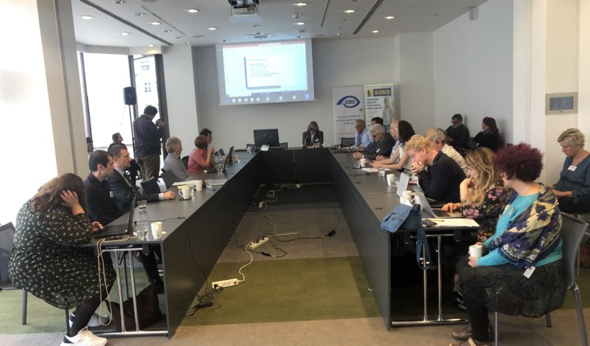 Uczestnicy na konferencji Europejskiej Unii Niewidomych siedzą przy stole w kształcie litery U.