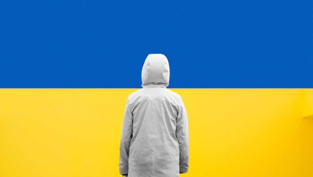 Osoba w kapturze stoi na tle ukraińskiej flagi
