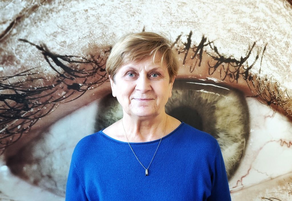 Elżbieta Oleksiak, ubrana w niebiską sukienkę. Uśmiecha się lekko do zdjęcia.