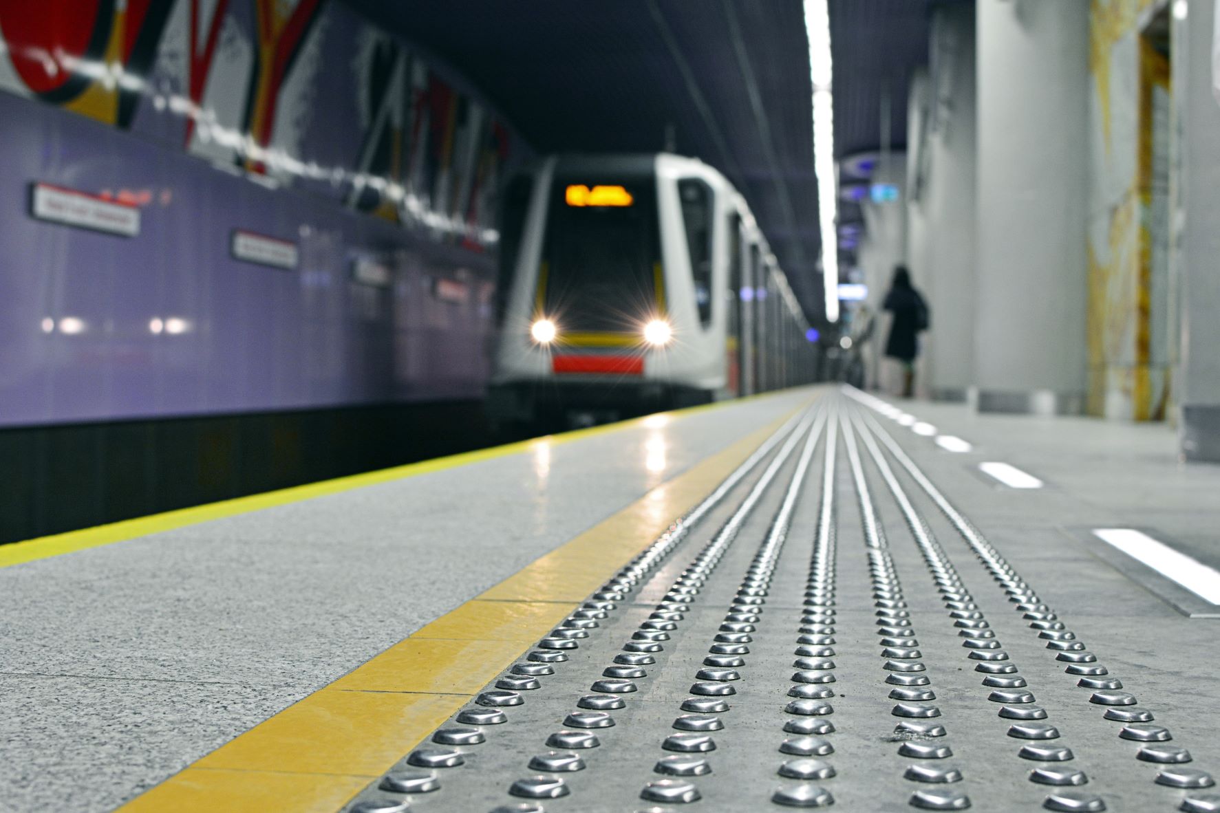 Peron metra w oddali pociąg, widać ścieżkę dotykową