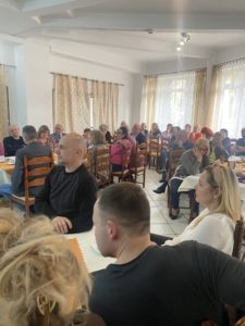 Sala szkoleniowa wypełniona uczestnikami, którzy siedzą przy stołach.
