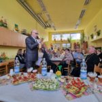 prezes koła stoi przed mikrofonem i czyta tekst z kartki, wita gości, pozostali siedzą i słuchają
