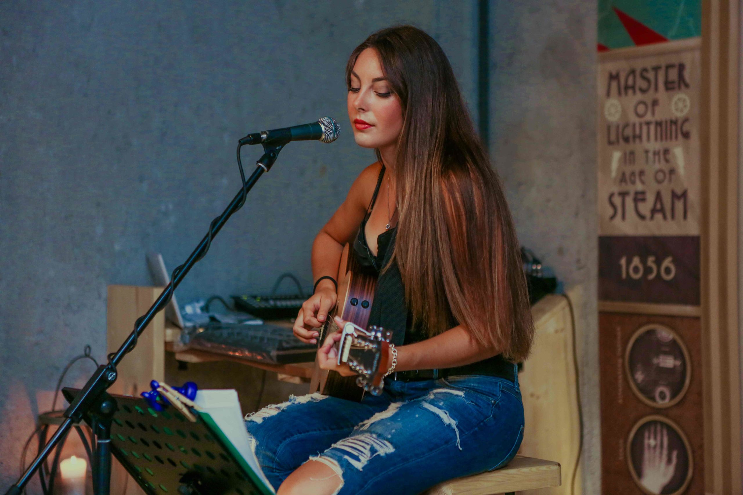 Dziewczyna z gitarą śpiewa do mikrofonu siedząc w pomieszczeniu