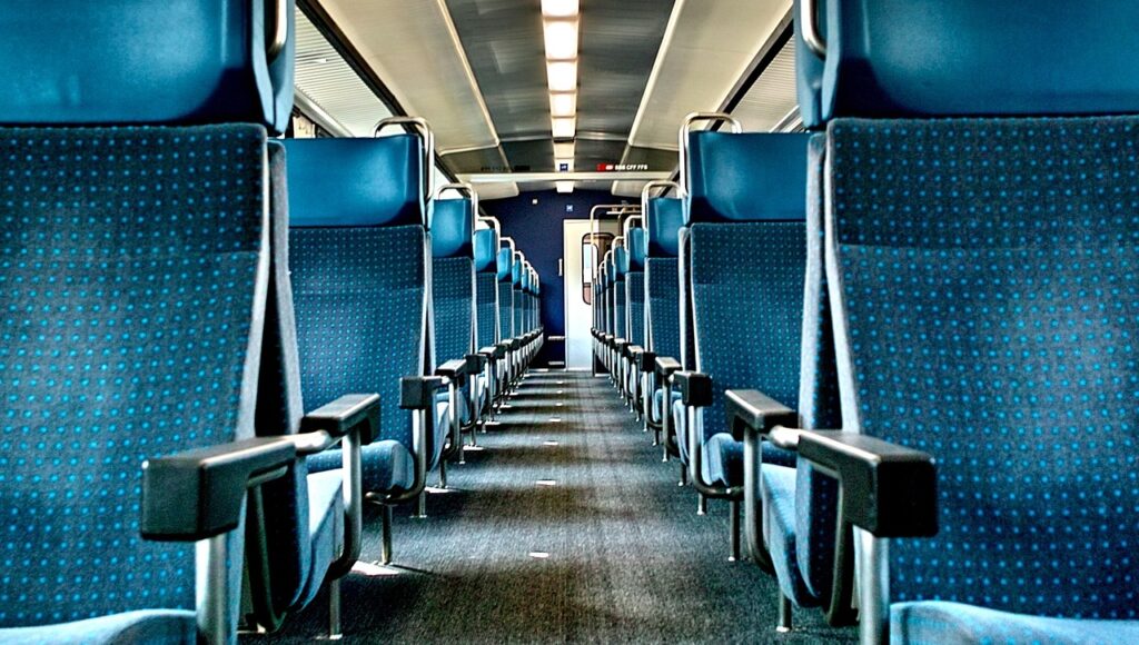 Wnętrze wagonu pociągu. Widok wąskiego przejścia pomiędzy fotelami.