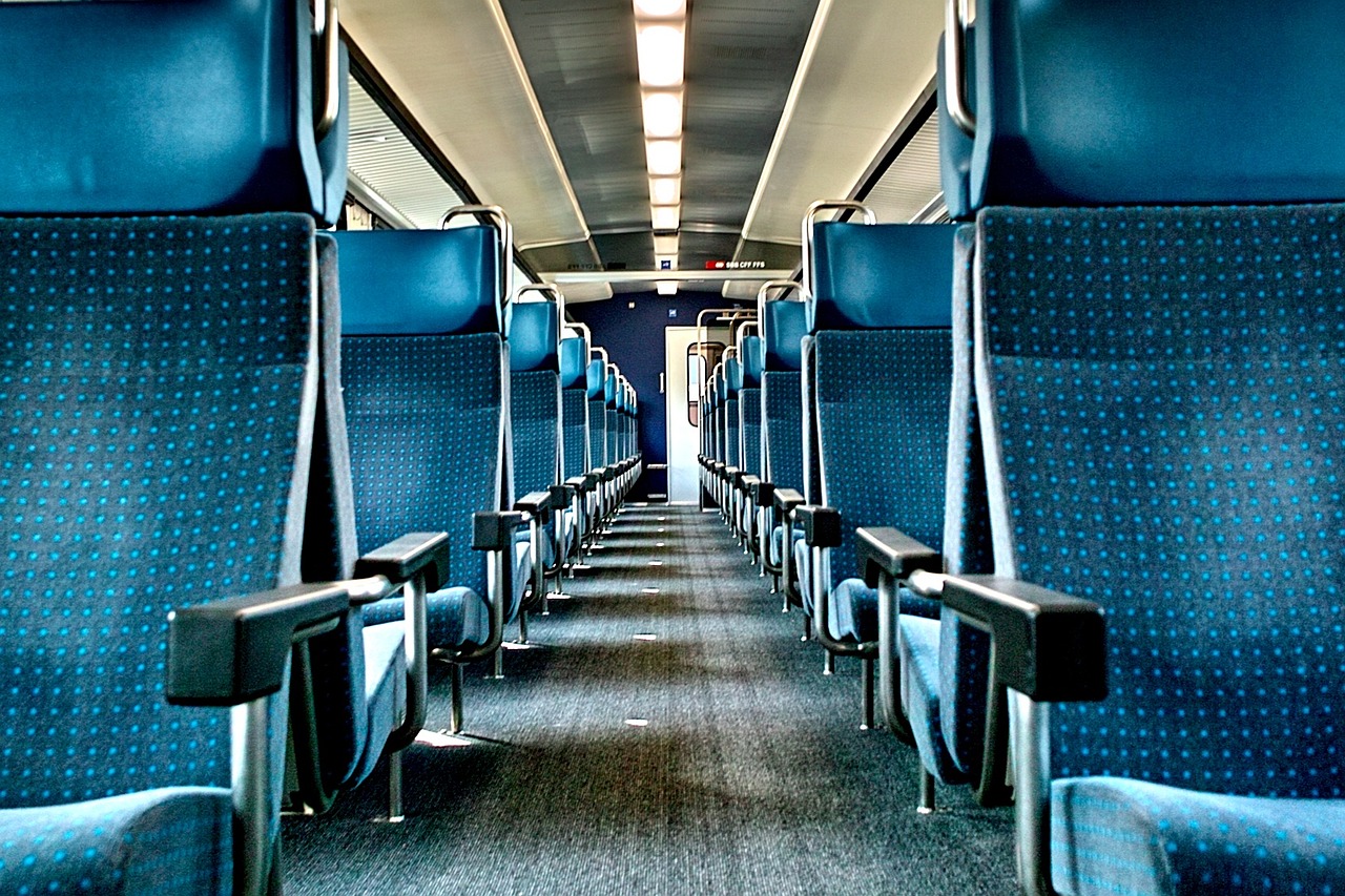 Wnętrze wagonu pociągu. Widok wąskiego przejścia pomiędzy fotelami.