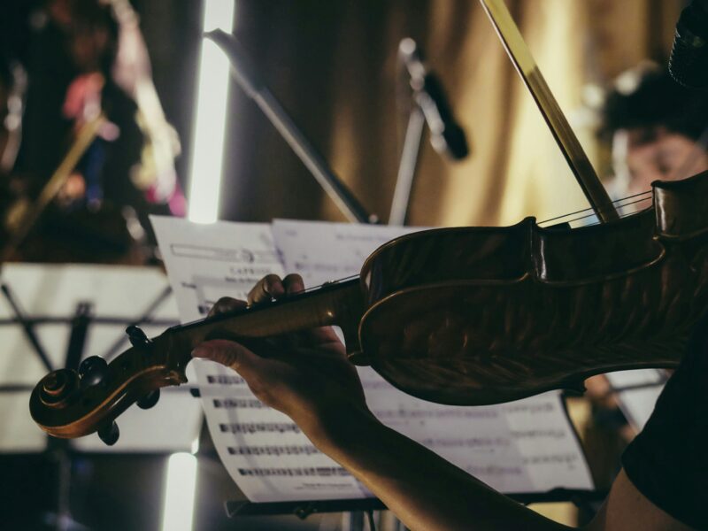 Widok na skrzypce, na których gra muzyk na koncercie, w tle nuty.