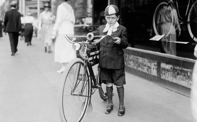 Mały chłopiec stoi obok roweru z wielkimi kołami. Fotografia archiwalna.