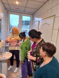Instruktorka pokazuje kursantkom, jak nakładać pastę na szczoteczkę do zębów.