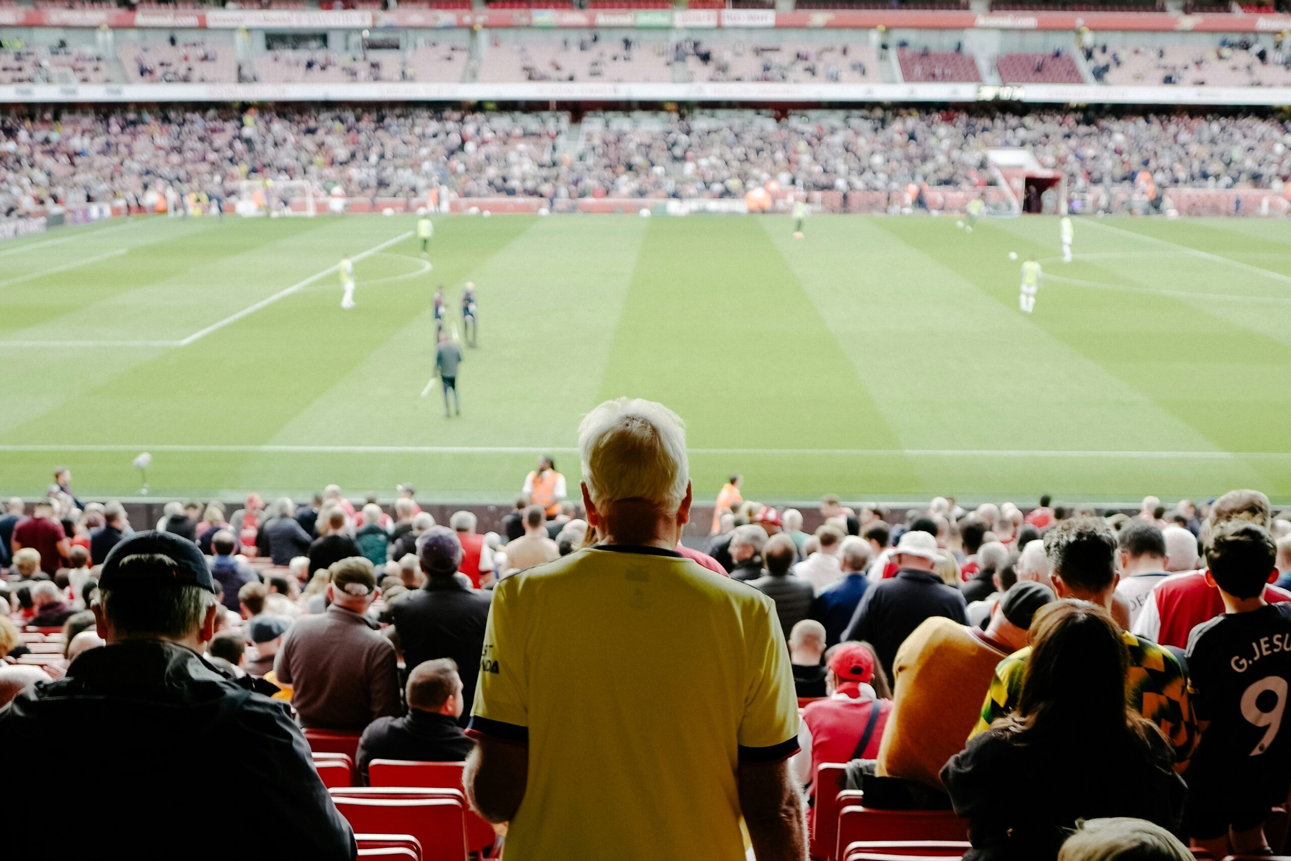 Kibice dopingują swoją drużynę piłkarską, w tle piłkarze rozgrywający mecz na stadionie.