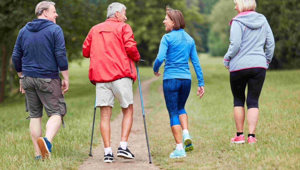 Czwórka seniorów w strojach sportowych idzie ścieżką leśną.